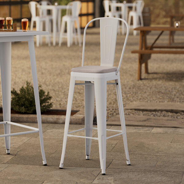 A Lancaster Table & Seating white outdoor cafe barstool with a gray cushion on a table outdoors.