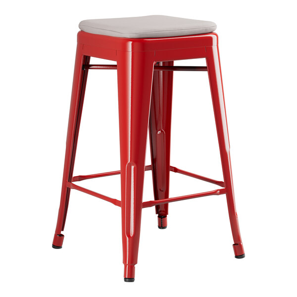 A red metal Lancaster Table & Seating backless counter height stool with a gray cushion.
