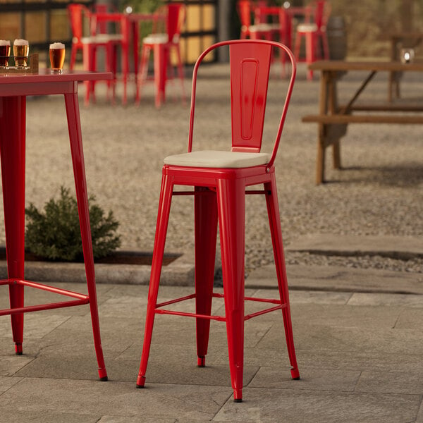 A Lancaster Table & Seating red outdoor bar stool with a tan cushion on a table.