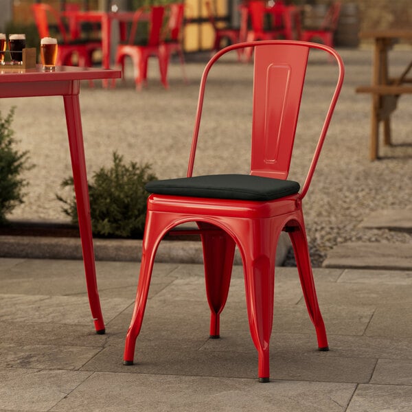 A red Lancaster Table & Seating outdoor cafe chair with a black cushion on a patio.