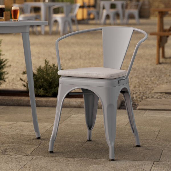 A Lancaster Table & Seating gray metal outdoor arm chair with a white cushion on a patio.