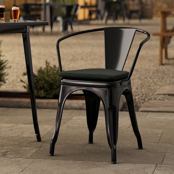 A Lancaster Table & Seating black outdoor arm chair with a black cushion on a patio table.