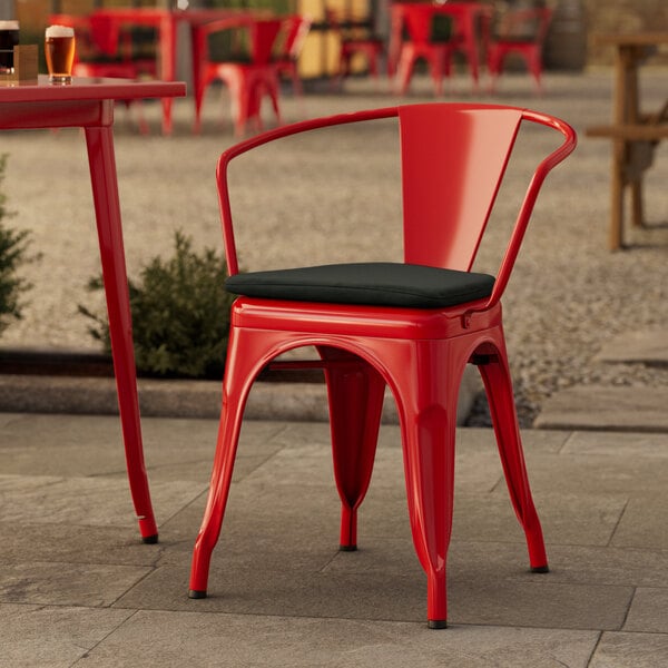 A red Lancaster Table & Seating outdoor arm chair with a black cushion on a patio.