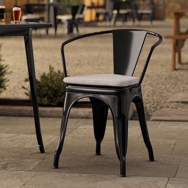 A Lancaster Table & Seating black outdoor arm chair with a gray cushion on a patio.
