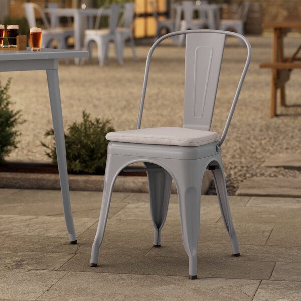 A Lancaster Table & Seating gray metal outdoor cafe chair with a gray fabric cushion on a stone patio.