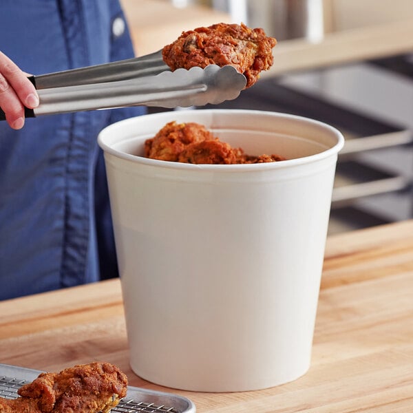 A person holding tongs to a white Innopak food bucket.