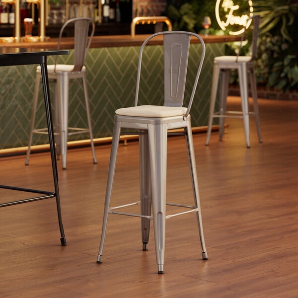 A Lancaster Table & Seating silver barstool with a tan cushion on a wood floor.