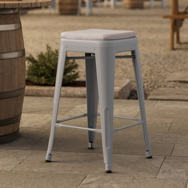 A gray metal outdoor backless counter height stool with a gray cushion on a stone surface.