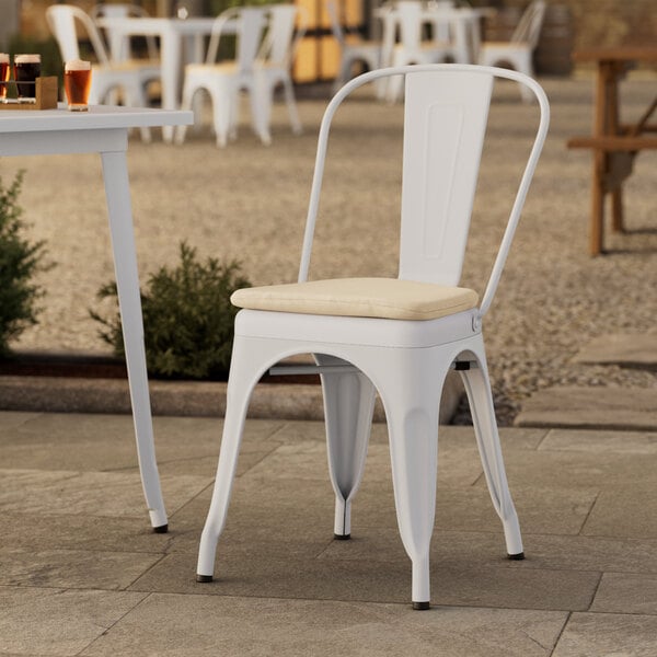 A Lancaster Table & Seating white outdoor cafe chair with a tan cushion on a patio table.