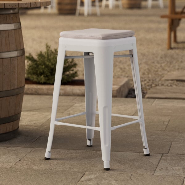 A Lancaster Table & Seating white outdoor backless counter height stool with a gray cushion on a stone surface.