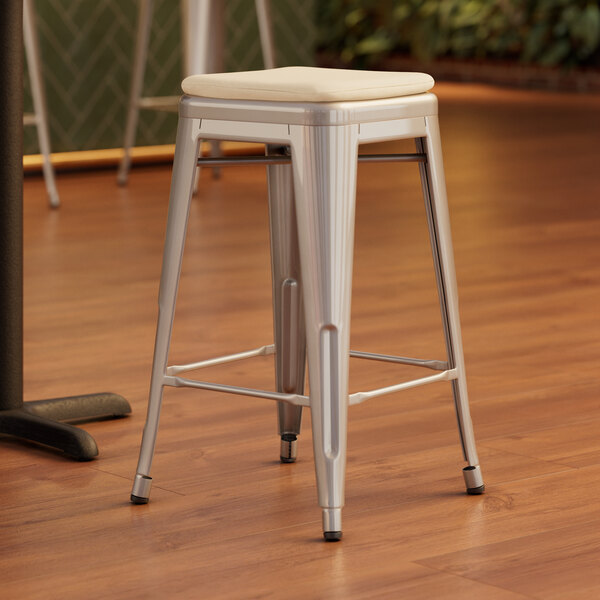A Lancaster Table & Seating silver metal backless counter height stool with a white cushion on top.