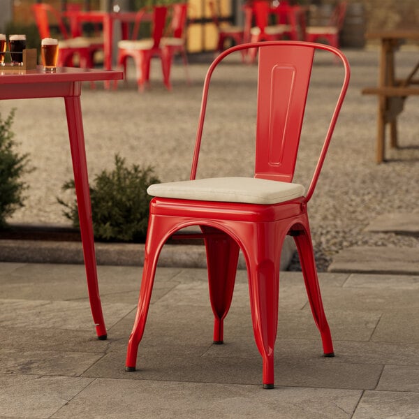 A red metal Lancaster Table & Seating outdoor cafe chair with a tan cushion on a patio.
