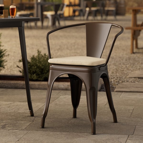 A Lancaster Table & Seating brown metal outdoor arm chair with a tan cushion on a patio.