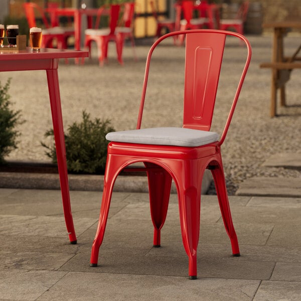 A red metal Lancaster Table & Seating outdoor cafe chair with a gray cushion.