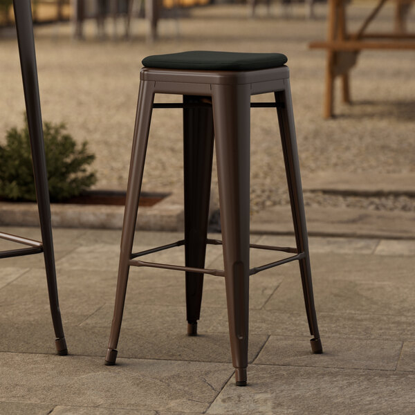 A pair of Lancaster Table & Seating copper outdoor bar stools with black fabric cushions on a stone surface.