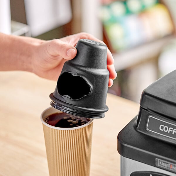 A hand using a black KleanTake lid applicator to put a black lid on a coffee cup.