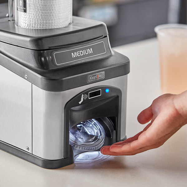 A hand using a KleanTake lid dispenser on a counter.