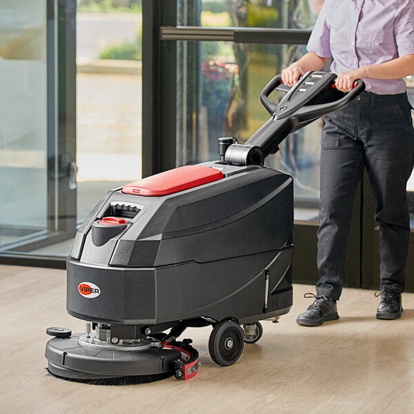A woman using a Viper walk behind floor scrubber to clean a floor in a professional kitchen.