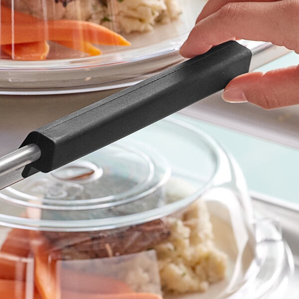 A hand holding a black Baker's Mark silicone bun / sheet pan clip.