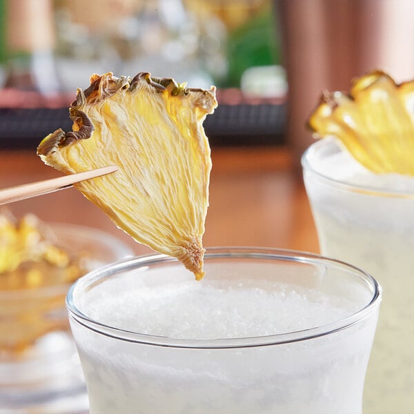 A dried pineapple quarter slice being dipped into a glass of white liquid.