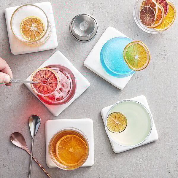 A hand using tweezers to add a dried citrus slice to a blue and orange drink.