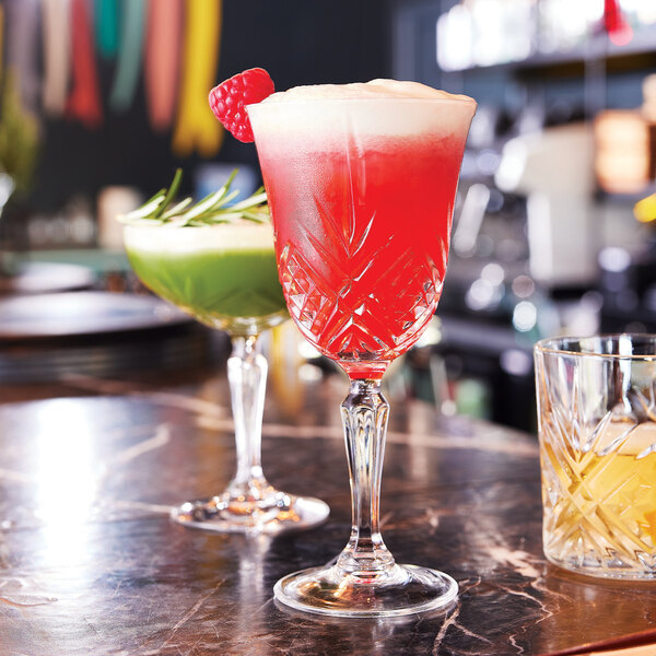 Two Arcoroc Broadway cocktail glasses filled with a red drink on a table.