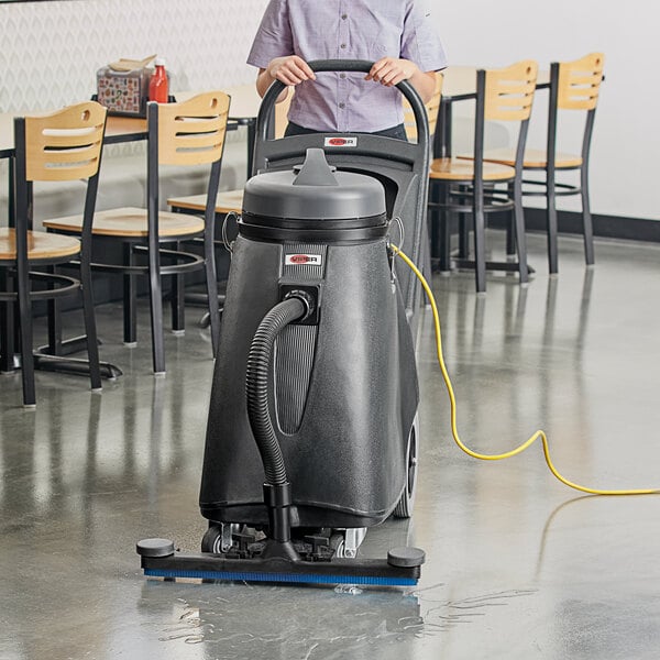 A woman using a Viper Shovelnose wet/dry vacuum to clean a floor in a room with chairs and tables.