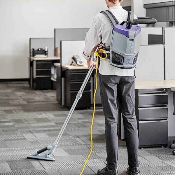 A man wearing a ProTeam GoFit backpack vacuum cleaner in a corporate office cafeteria.