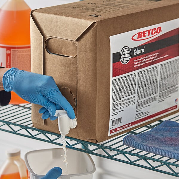 A person in blue gloves pouring Betco Glare floor finish into a box.