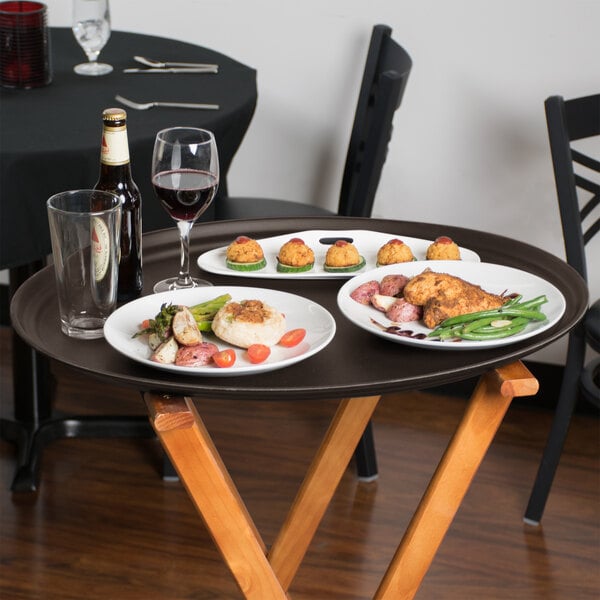 A Tavern Tan Cambro non-skid oval serving tray with plates of food and wine on a wooden table.