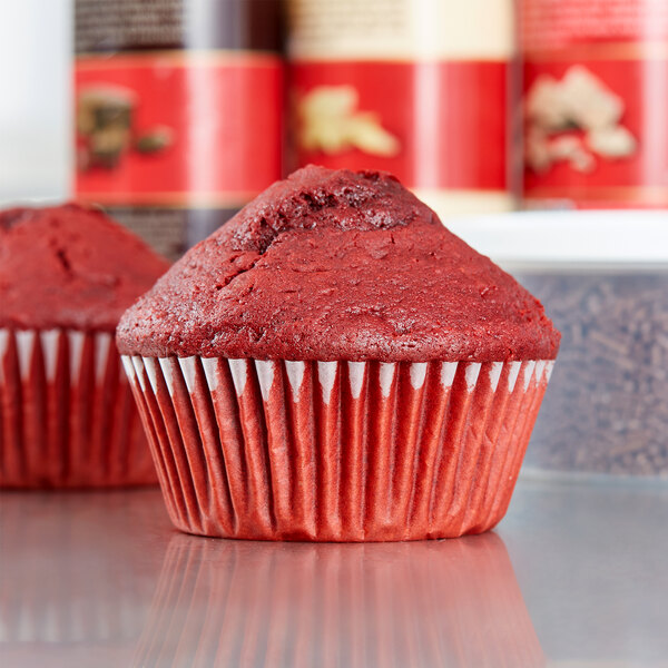 A red cupcake in a Hoffmaster white fluted baking cup.