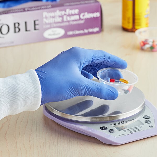 A gloved hand holding a plastic container of pills.