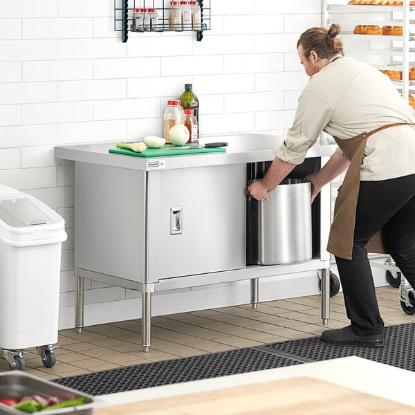 A man in an apron pushing a Steelton stainless steel enclosed base table with sliding doors.