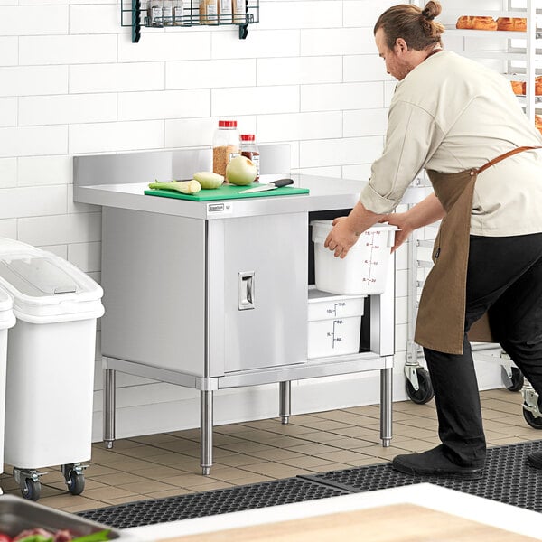 A man in a black apron using a Steelton stainless steel enclosed base table to hold a white container.