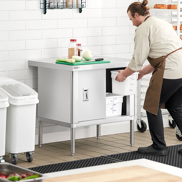 A man in a chef's uniform opening a Steelton stainless steel table with sliding doors.