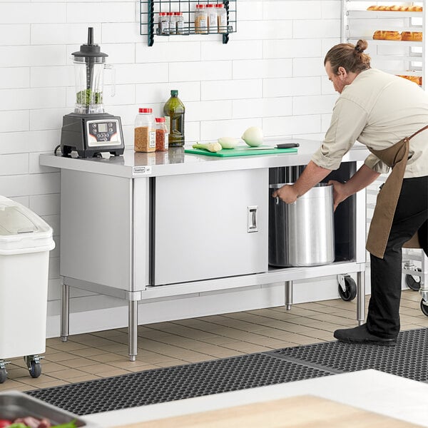 A woman using a Steelton stainless steel enclosed base table in a professional kitchen to prepare food.