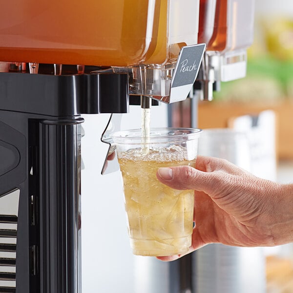 A person holding a cup of Tractor Beverage Co. peach drink concentrate.
