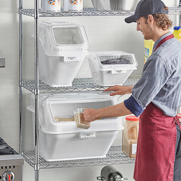 A man in a red apron putting food into Baker's Lane ingredient containers on a shelf.