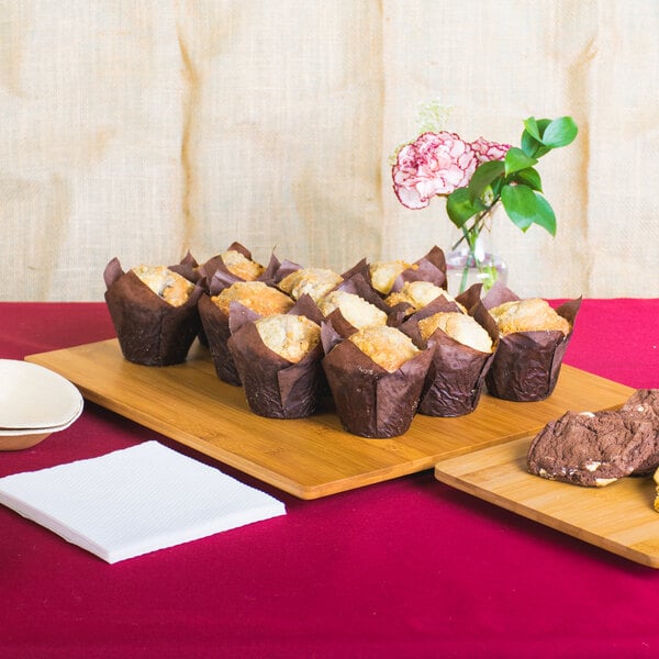 An American Metalcraft square bamboo platter on a table with a tray of muffins and a plate of cookies.
