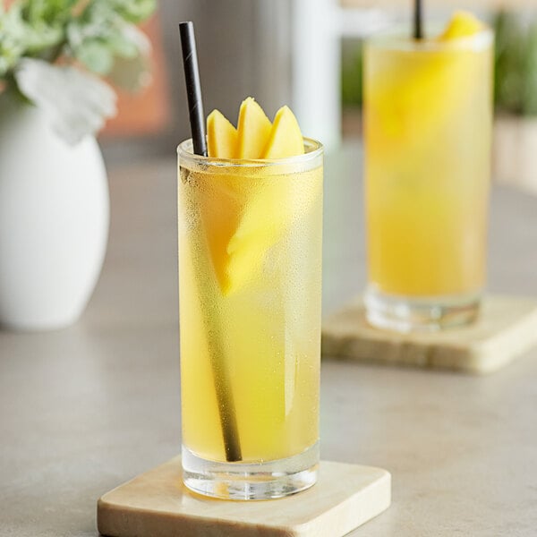 A glass of Tractor Beverage Co. Organic Mango juice with a straw.