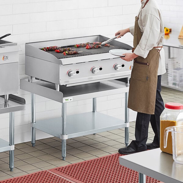 A man in a brown apron cooking food on a Cooking Performance Group radiant charbroiler.