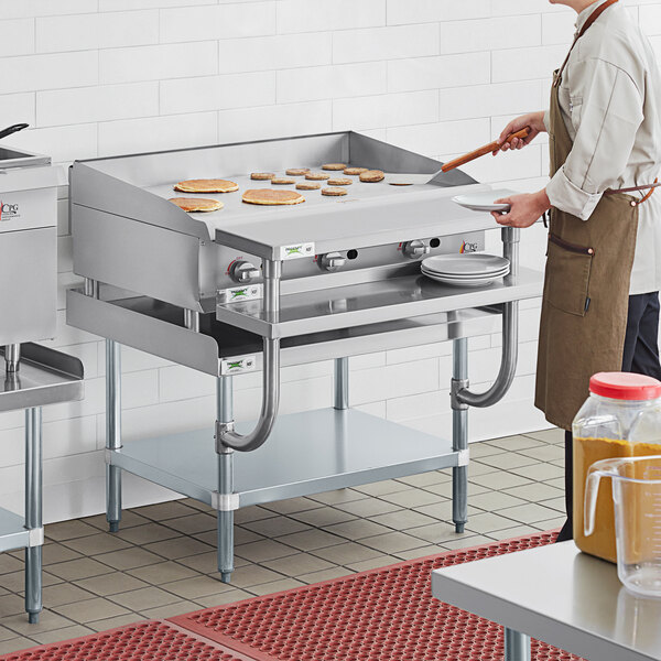 A man wearing a brown apron cooking food on a large metal surface on a stainless steel counter.