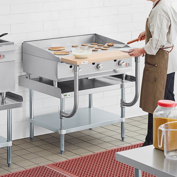 A man in a brown apron using a Cooking Performance Group Thermostatic Griddle on a Regency chef station.