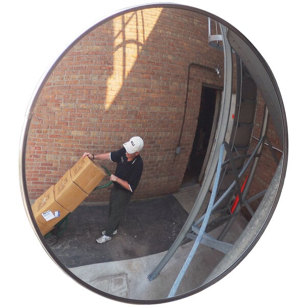 A man pushing a cart with boxes in front of a Vestil outdoor convex mirror.