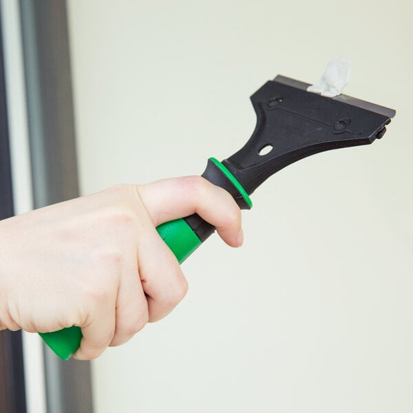 A hand holding a Unger ErgoTec scraper with a green handle.