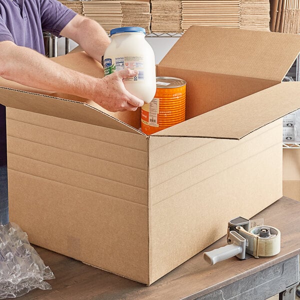 A person holding a Lavex Kraft shipping box with a jug of milk and canned food inside.