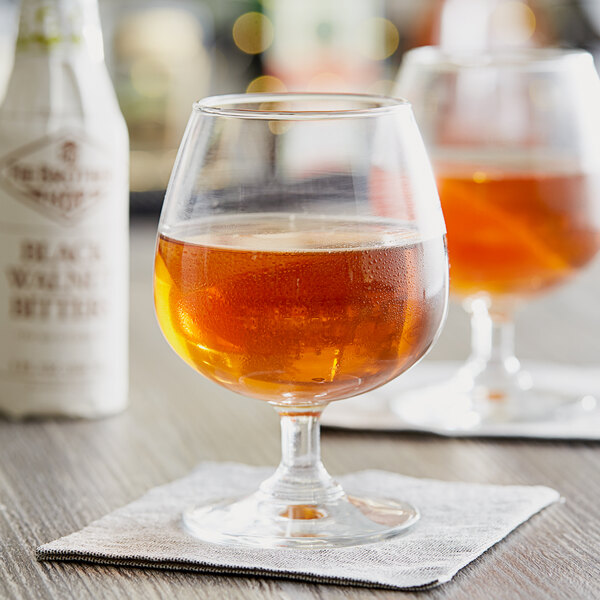 A bottle of Fee Brothers Black Walnut Bitters on a table next to two glasses of brown liquid.
