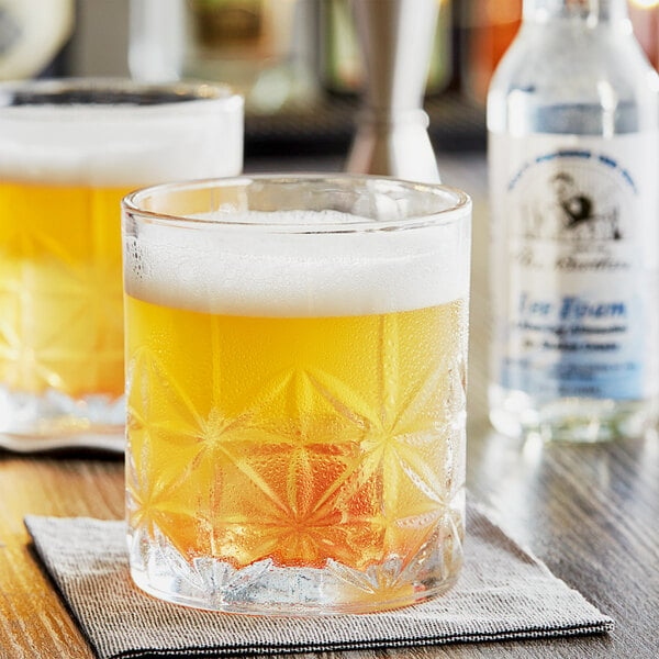 A close-up of a can of Fee Brothers Cocktail Foam on a table with two glasses of orange drinks.