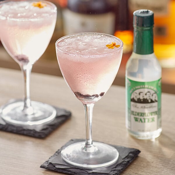 A bottle of Fee Brothers Elderflower Water next to two glasses of pink liquid.