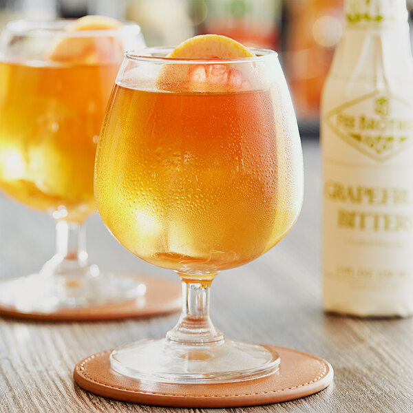 A close-up of a glass of a cocktail with a bottle of Fee Brothers Grapefruit Bitters.